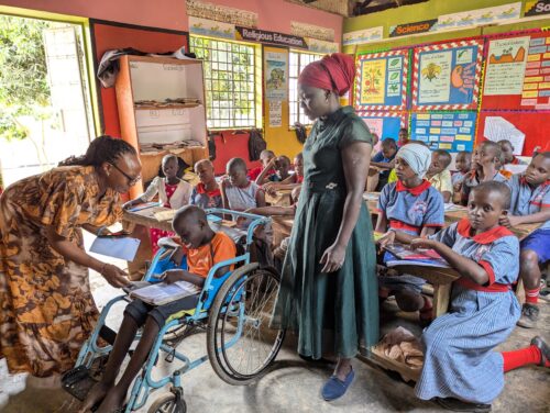 Photo of educators and pupils in a colourful and bright classroom, with a child in a wheelchair at the front