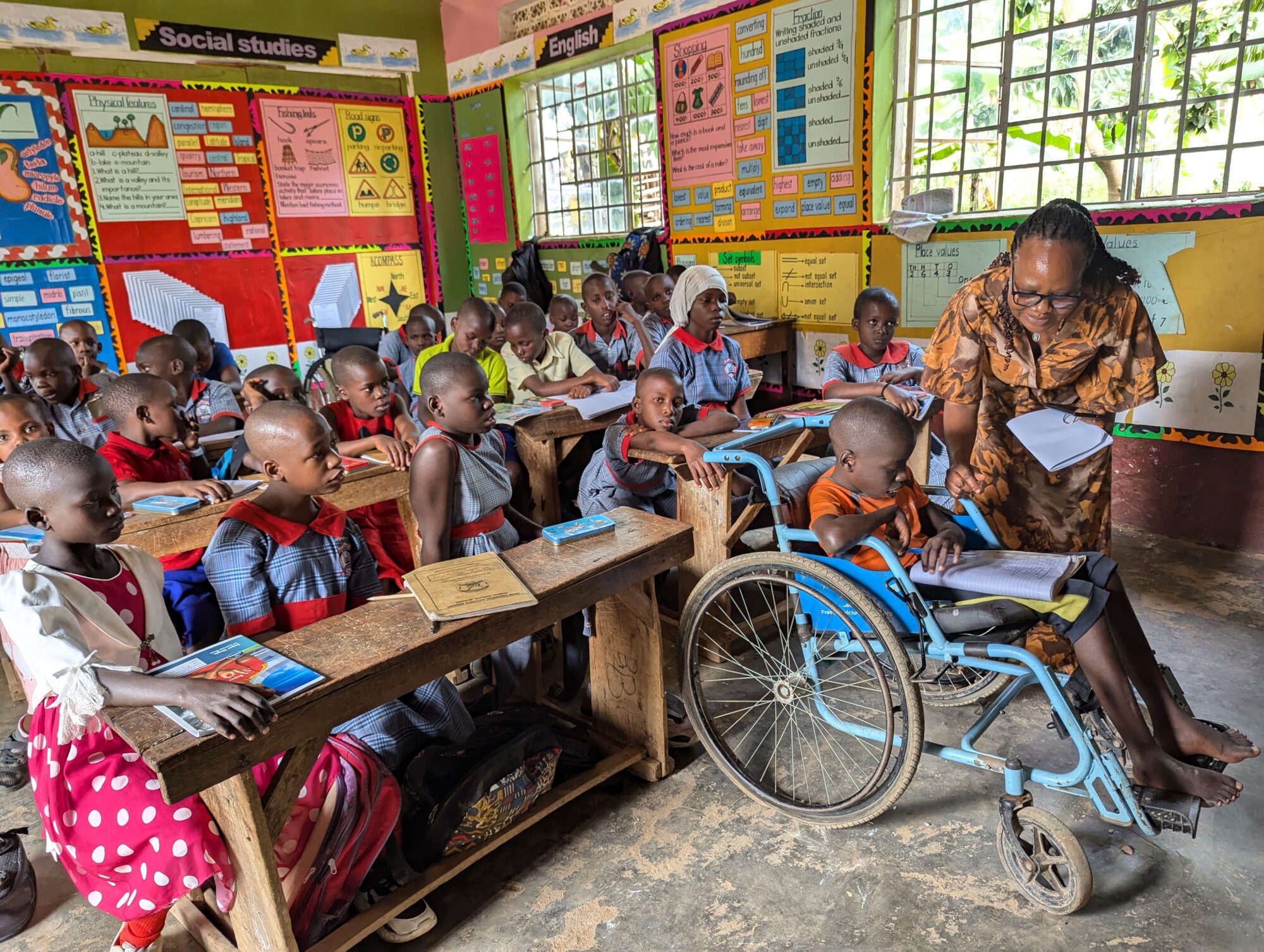 Nakkazi and Matinyi, special needs education teachers at Good Samaritan Inclusive Primary School giving individualised support to a disabled student to allow him learn at his own pace, together with other students