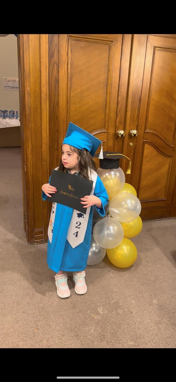 Melia’s graduation ceremony from kindergarten where she held her graduation certificate and wore her graduation outfit. Picture taken by Narin Mohammad in June 2024
