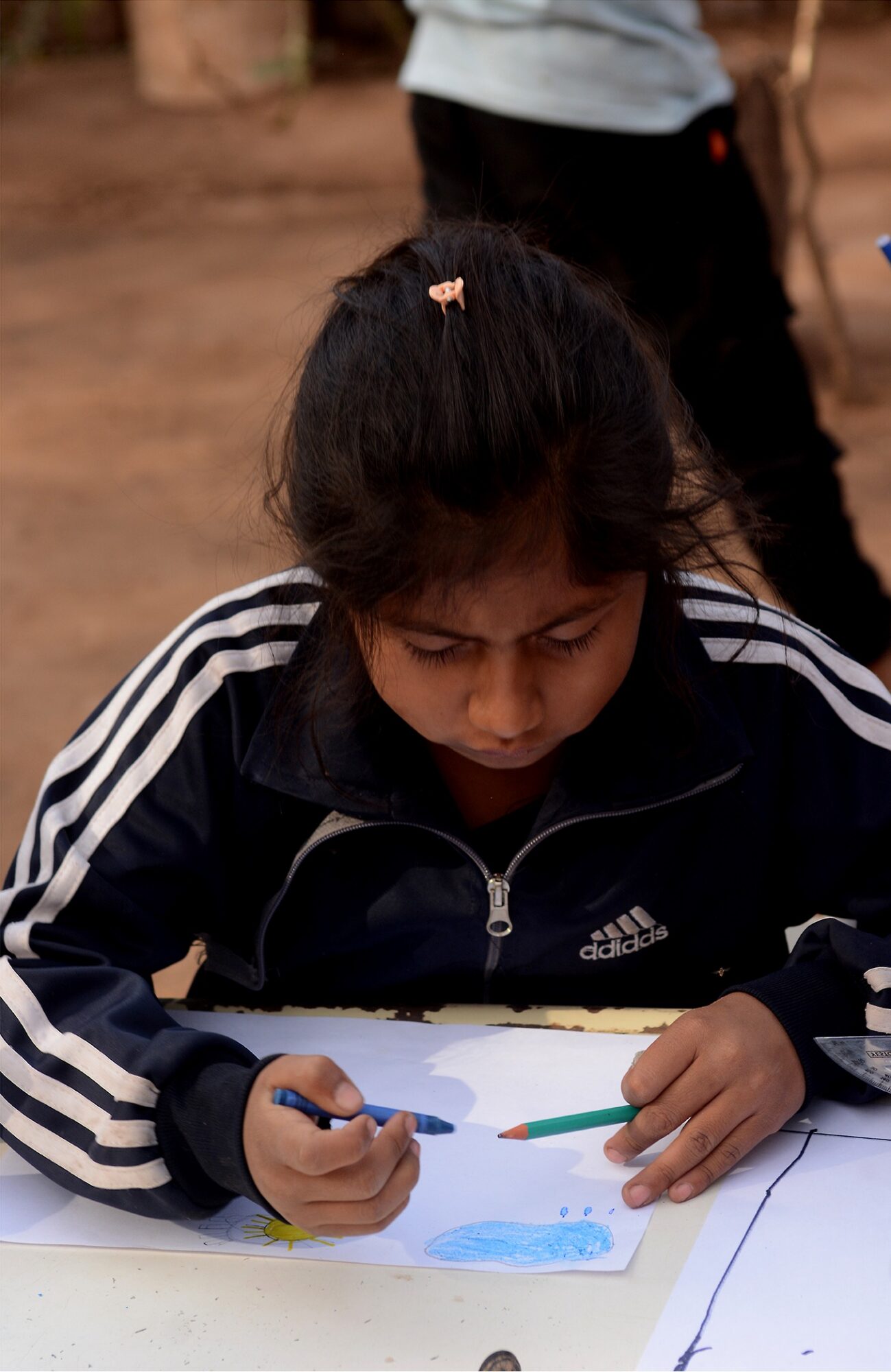 A student works on a drawing in the yard at Matche Ta ïs, where activities often take place outdoors. Photograph by Gabriel Borndones.