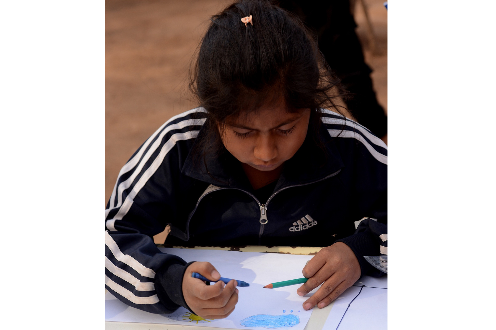 A student works on a drawing in the yard at Matche Ta ïs, where activities often take place outdoors. Photo by Gabriel Borndones.